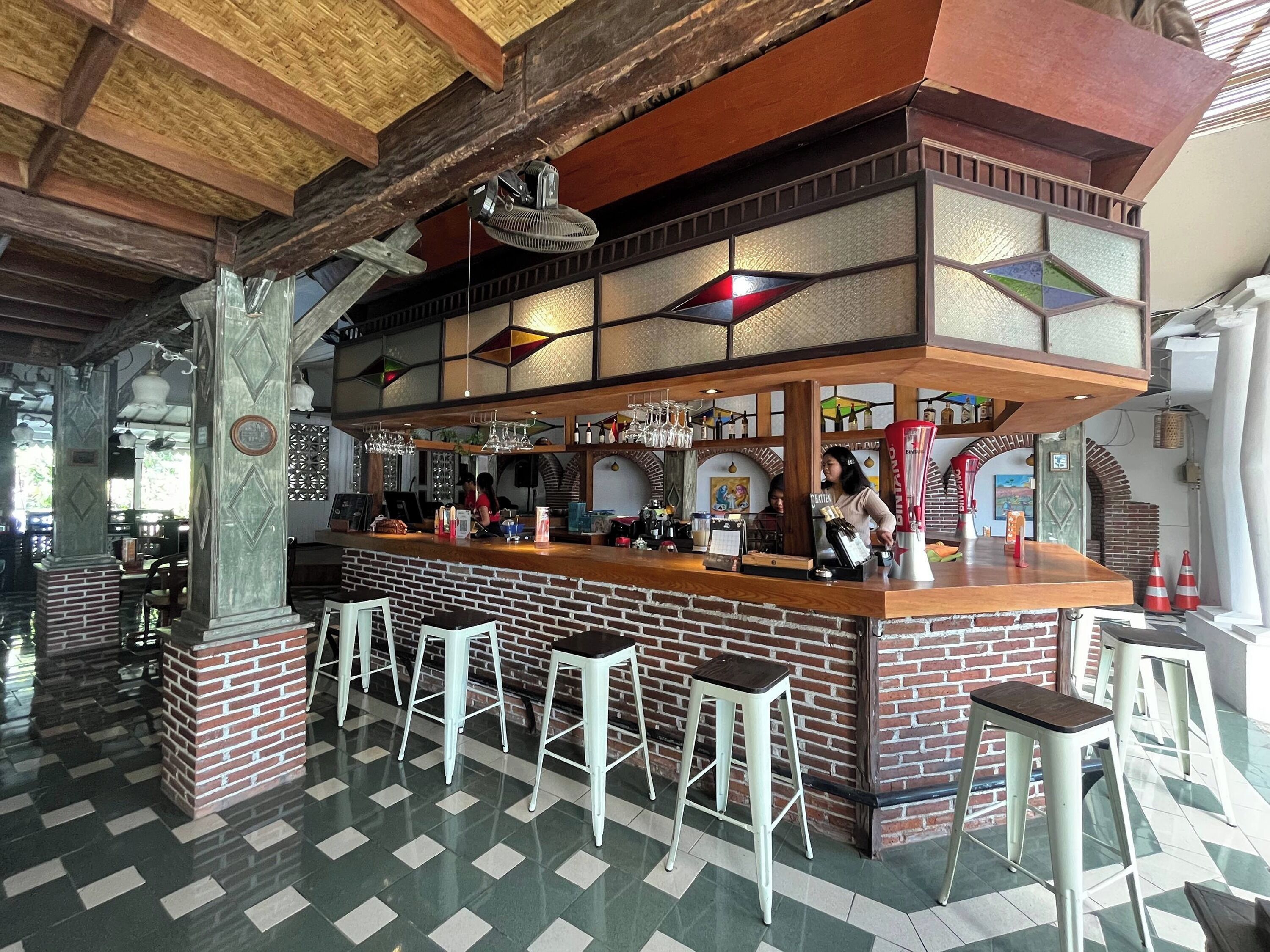 A bar area with a brick counter, stools, and hanging lights.