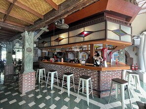 A bar area with a brick counter, stools, and hanging lights. - Attara Hostel Senggigi (Senggigi)