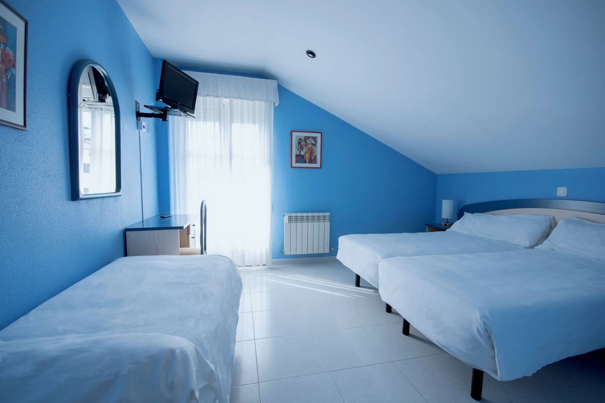 Un dormitorio con dos camas, un televisor montado en la pared, una ventana con cortinas y un radiador.