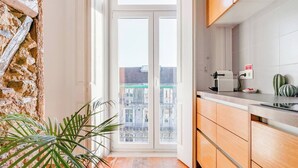 A modern kitchen with wooden cabinets, a built-in oven, and a view of the city through a glass door. - Eighteen21 Houses - Casa de São Paulo (Lisbon)