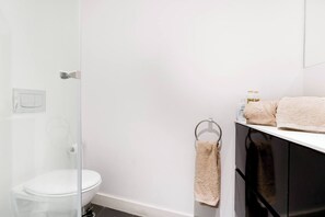A bathroom with a toilet, a glass shower enclosure, a towel rack with a towel, and a shelf with toiletries. - Eighteen21 Houses - Casa de São Paulo (Lisbon)