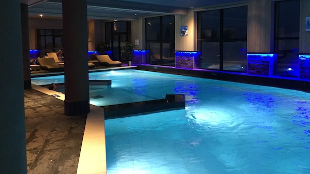 An indoor swimming pool with blue lighting, lounge chairs, and a stone accent wall.