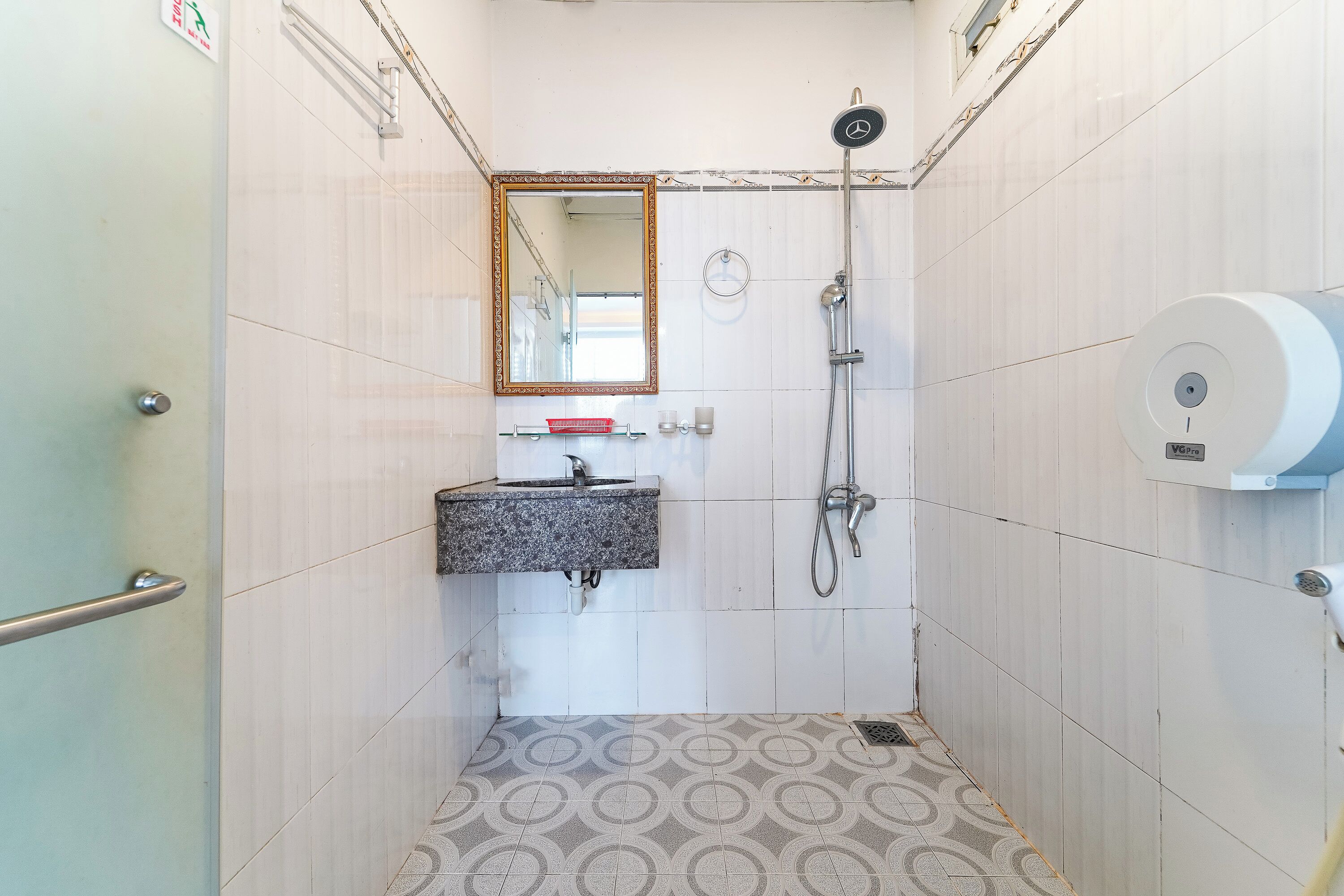A small bathroom with a sink, mirror, shower, and toilet paper dispenser.