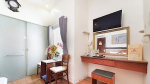 Una habitación con un escritorio de madera, una silla, un banco, un espejo, un reloj y una ventana con cortinas.
