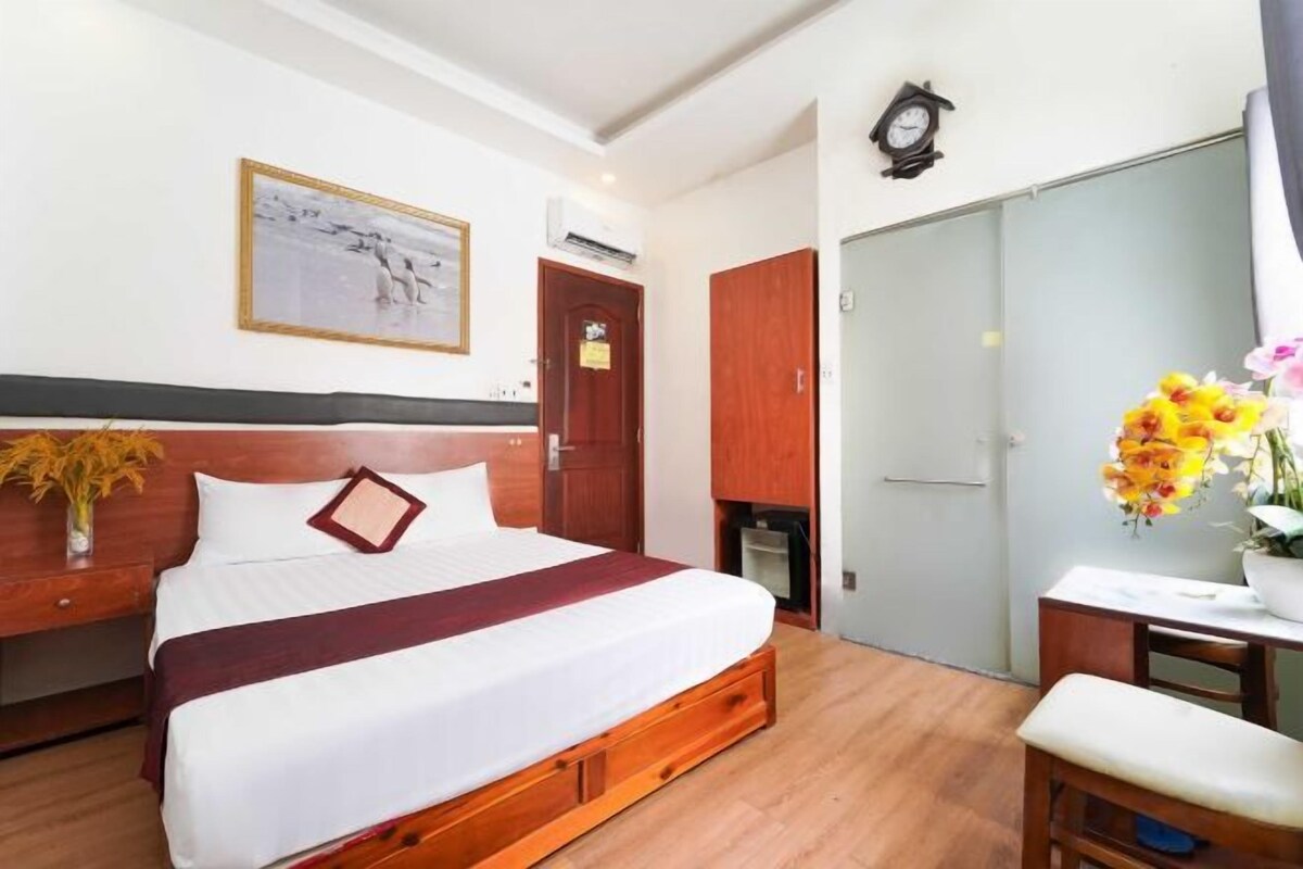 A hotel room with a bed, a desk, a chair, a wardrobe, and a clock on the wall.