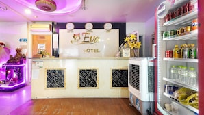 Zona de recepción de un hotel con un letrero de neón, un refrigerador lleno de bebidas y un pequeño santuario con una estatua.