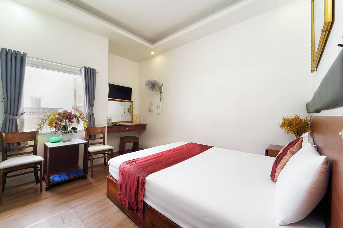 A hotel room with a bed, a desk, chairs, a mirror, and a window with curtains.