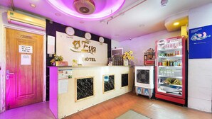 Zona de recepción de un hotel, con mostrador de recepción, un reloj, un refrigerador de Coca-Cola y una puerta con la leyenda 'Van Phong'.