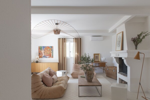 A modern living room with a beige sofa, a coffee table, and a fireplace. There is a painting on the wall and a vase with flowers on the table. - Maison Violette Paradou - pool - garden (Paradou)