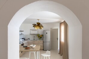 A modern kitchen with white cabinetry, a central island with a bowl and plates, a stainless steel refrigerator, and a unique leaf-shaped pendant light. - Maison Violette Paradou - pool - garden (Paradou)
