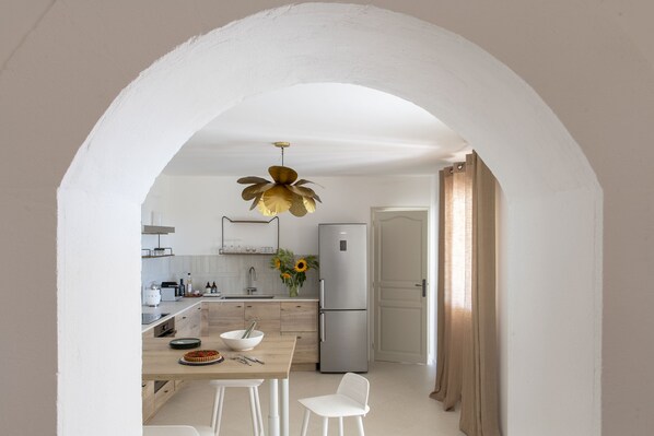A modern kitchen with white cabinetry, a central island with a bowl and plates, a stainless steel refrigerator, and a unique leaf-shaped pendant light.