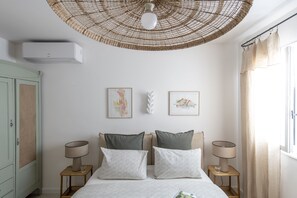 A bedroom with a bed, two bedside tables, a wall-mounted air conditioner, and two framed artworks. - Maison Violette Paradou - pool - garden (Paradou)