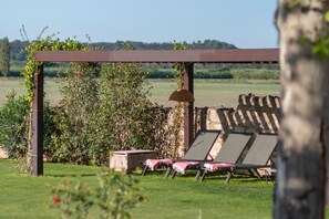 A garden with a pergola, a wooden shed, and lounge chairs.