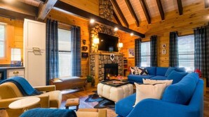 Ein gemütliches Blockhaus-Interieur mit Kamin aus Stein, einem darüber montierten Fernseher und einem blauen Sofagarnitur.