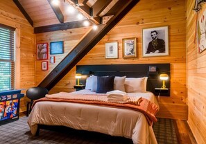 A cozy wooden cabin bedroom with a bed, two bedside lamps, and framed pictures on the wall.