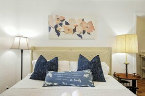 Un lit avec une tête de lit, deux lampes de chevet, une table de chevet et une œuvre d’art florale accrochée au mur.