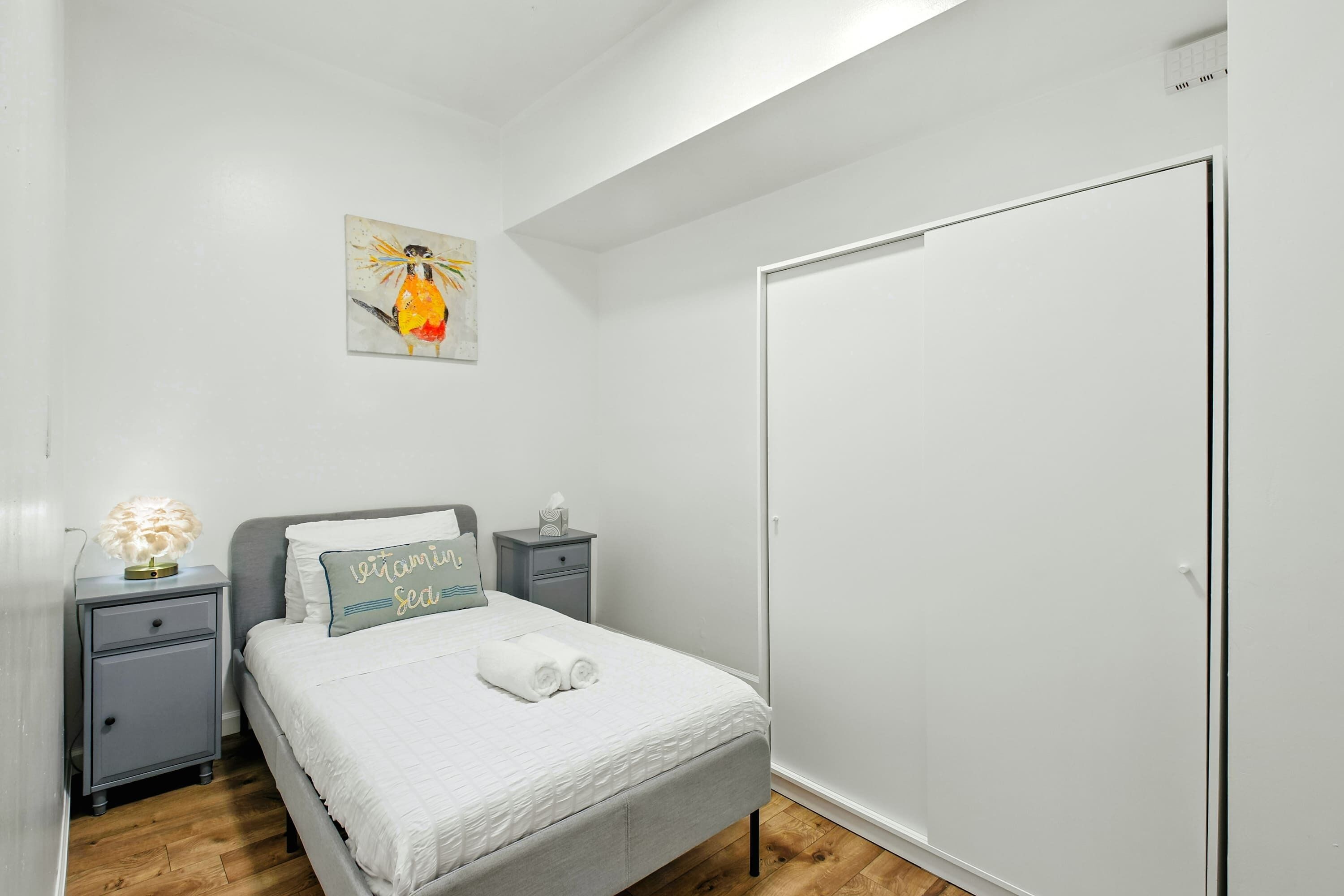 A bedroom with a bed, nightstands, a wall art piece, and a wardrobe.