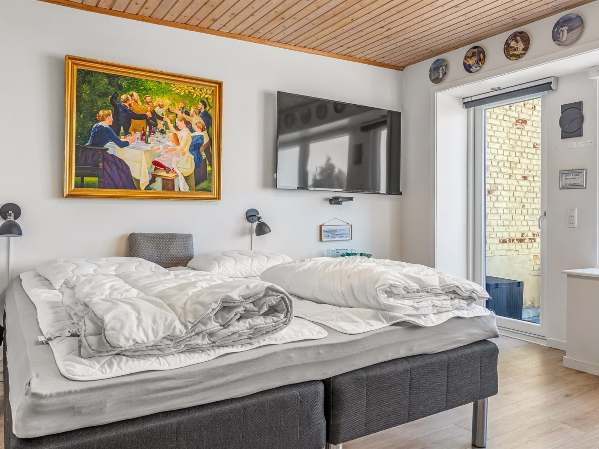 Ein Schlafzimmer mit einem Bett, einem Fernseher, einem Gemälde und einer Tür zu einem Außenbereich.