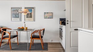 Une cuisine moderne avec des meubles blancs, une table à manger et deux chaises, ainsi qu’un luminaire suspendu.