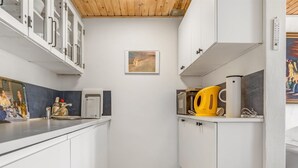 Une cuisine de taille réduite avec des meubles blancs, un plafond en bois et un petit tableau accroché au mur.