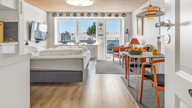 Une chambre moderne avec un lit, un bureau et une chaise. Une fenêtre offre une vue sur les immeubles et les arbres.