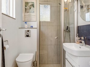 A bathroom with a toilet, a shower, and a sink. There is a framed picture on the wall and a small shelf with toiletries. - "Sibyll" - 2km from the sea by Interhome (Skagen)