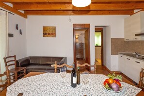 Una sala de estar con techo de madera, una mesa de comedor con mantel floral, un sofá y una zona de cocina con armarios y un lavabo.
