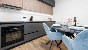 Une cuisine moderne équipée d’un four encastré, d’une machine à café et d’un coin repas avec deux chaises bleues et une table dressée pour deux personnes.