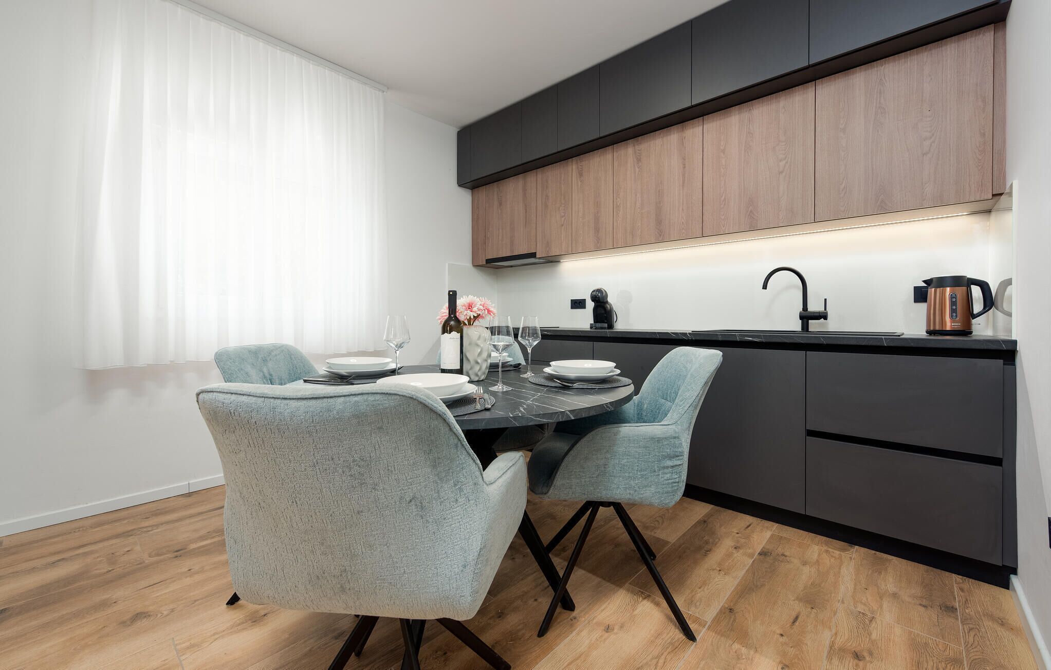 A modern kitchen with dark cabinets, a black countertop, and a wooden floor.