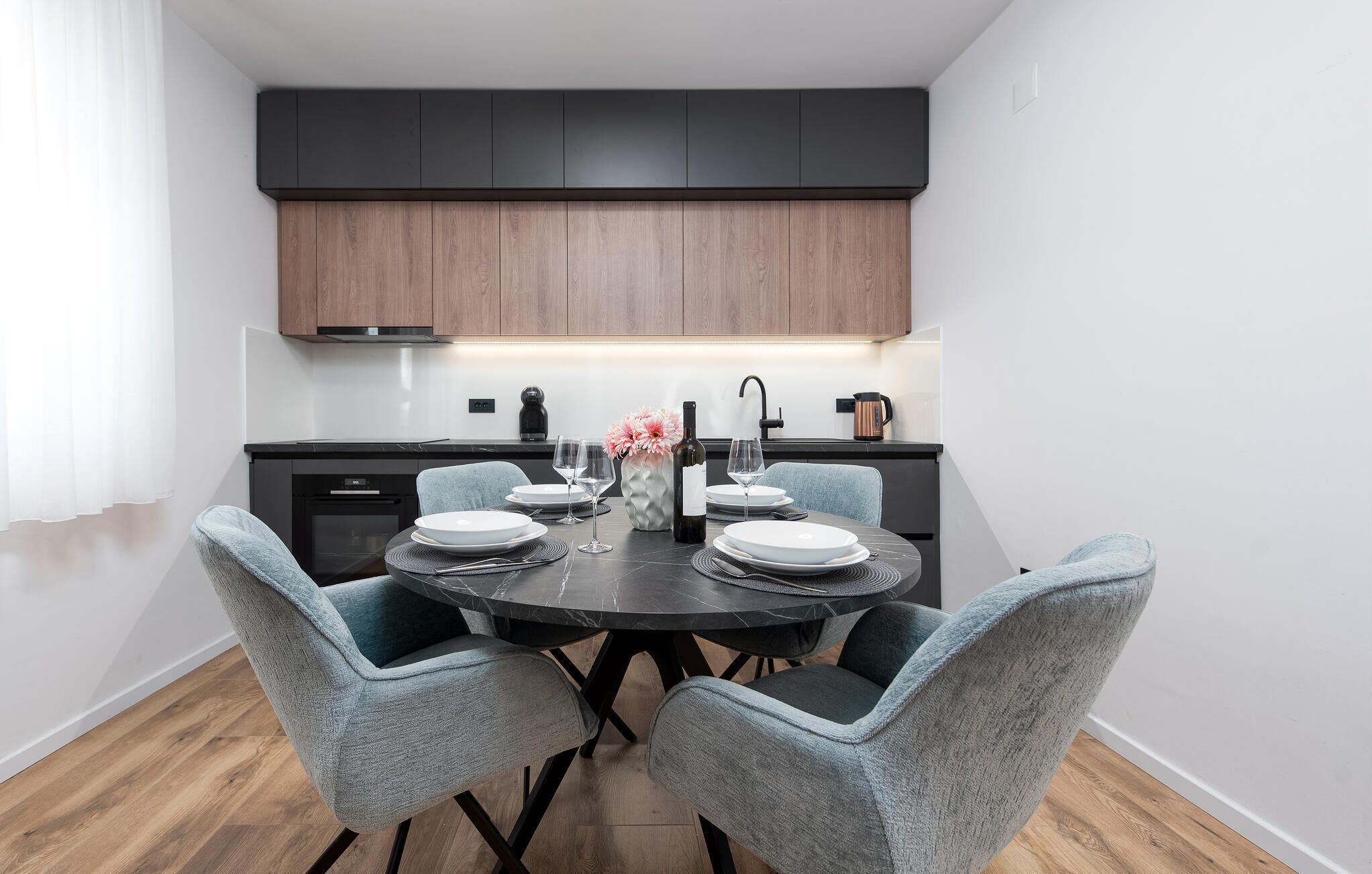 A modern kitchen with dark cabinets, a round dining table, and light blue chairs.
