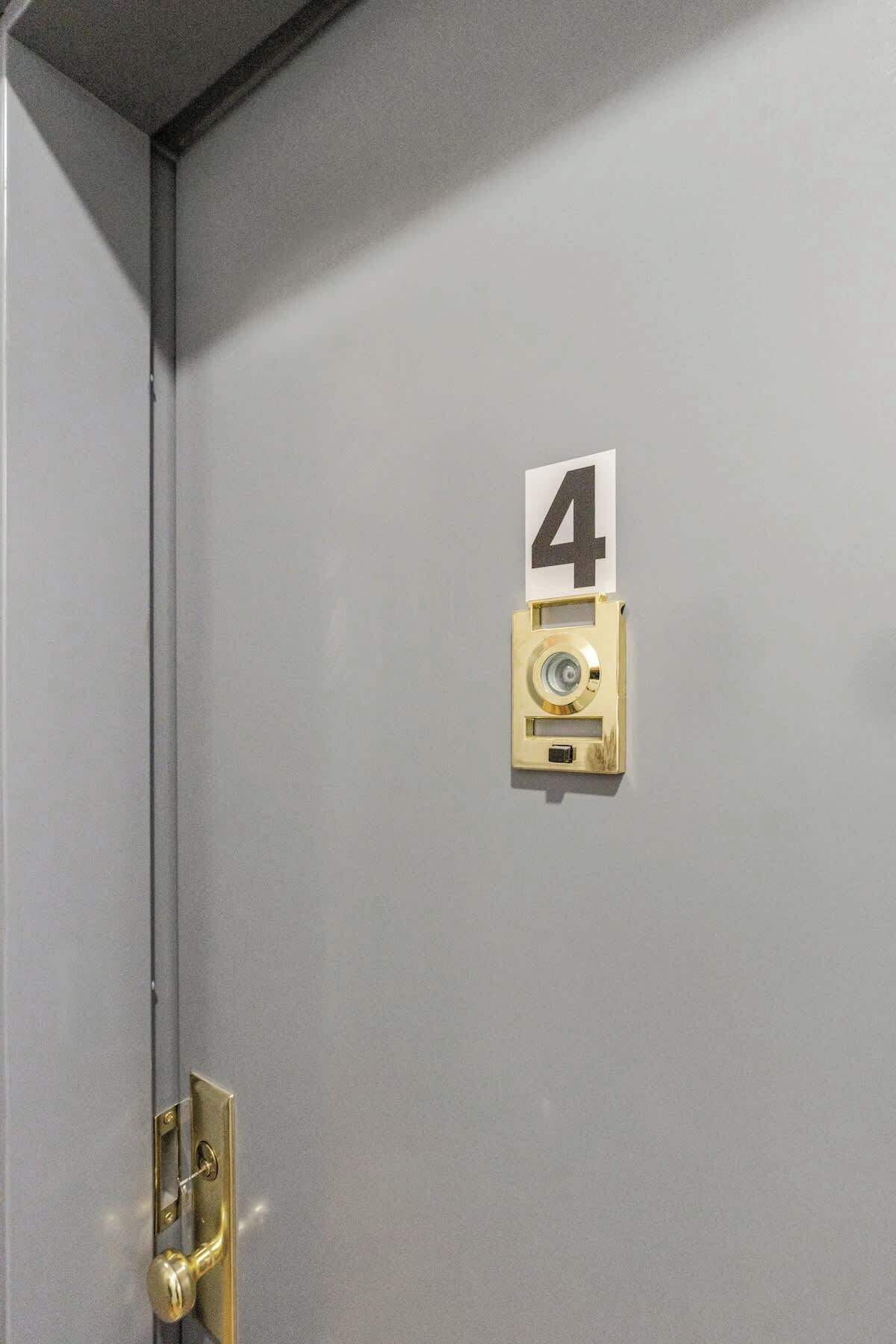Eine graue Tür mit Messingriegel und einem Schild, das die Zimmernummer 4 anzeigt.