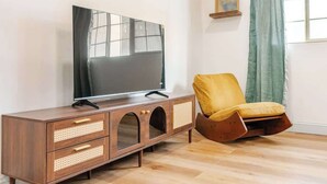 A living room with a wooden TV stand, a flat-screen TV, a yellow armchair, and a window with curtains. - Mins to Fishtown & Center City | GlobeNest (Philadelphia)
