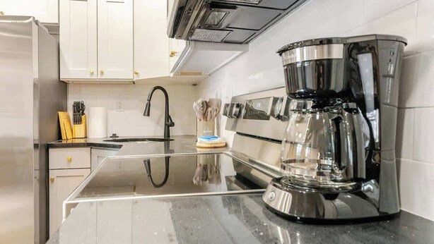 A modern kitchen with white cabinets, a stainless steel coffee maker, and a black countertop. - Mins to Fishtown & Center City | GlobeNest (Philadelphia)
