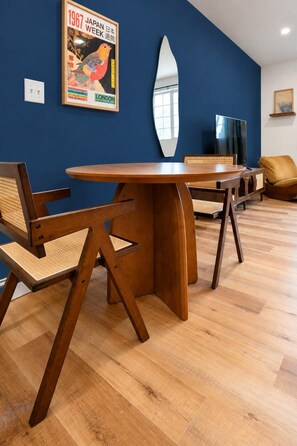 A room with a round wooden table, two chairs, a large mirror, and a poster on the wall.
