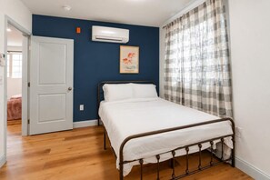 A bedroom with a bed, an air conditioning unit, a door, and a window with curtains.