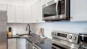Une cuisine moderne avec des armoires blanches, des appareils en acier inoxydable, un four à micro-ondes et une machine à café.