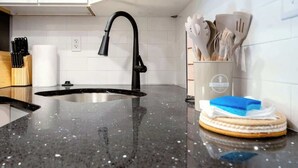Une cuisine dotée d’un plan de travail en granit noir, d’un robinet noir et d’un ensemble d’ustensiles de cuisine en bois rangés dans un porte-ustensiles.