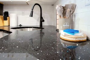 A kitchen with a black granite countertop, a black faucet, and a set of wooden utensils in a holder. - Mins to Fishtown & Center City | GlobeNest (Philadelphia)