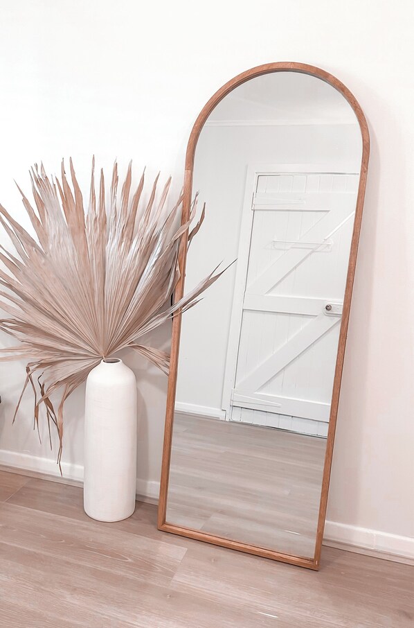 A mirror with a wooden frame, a white vase with dried plants, and a white door in the background.