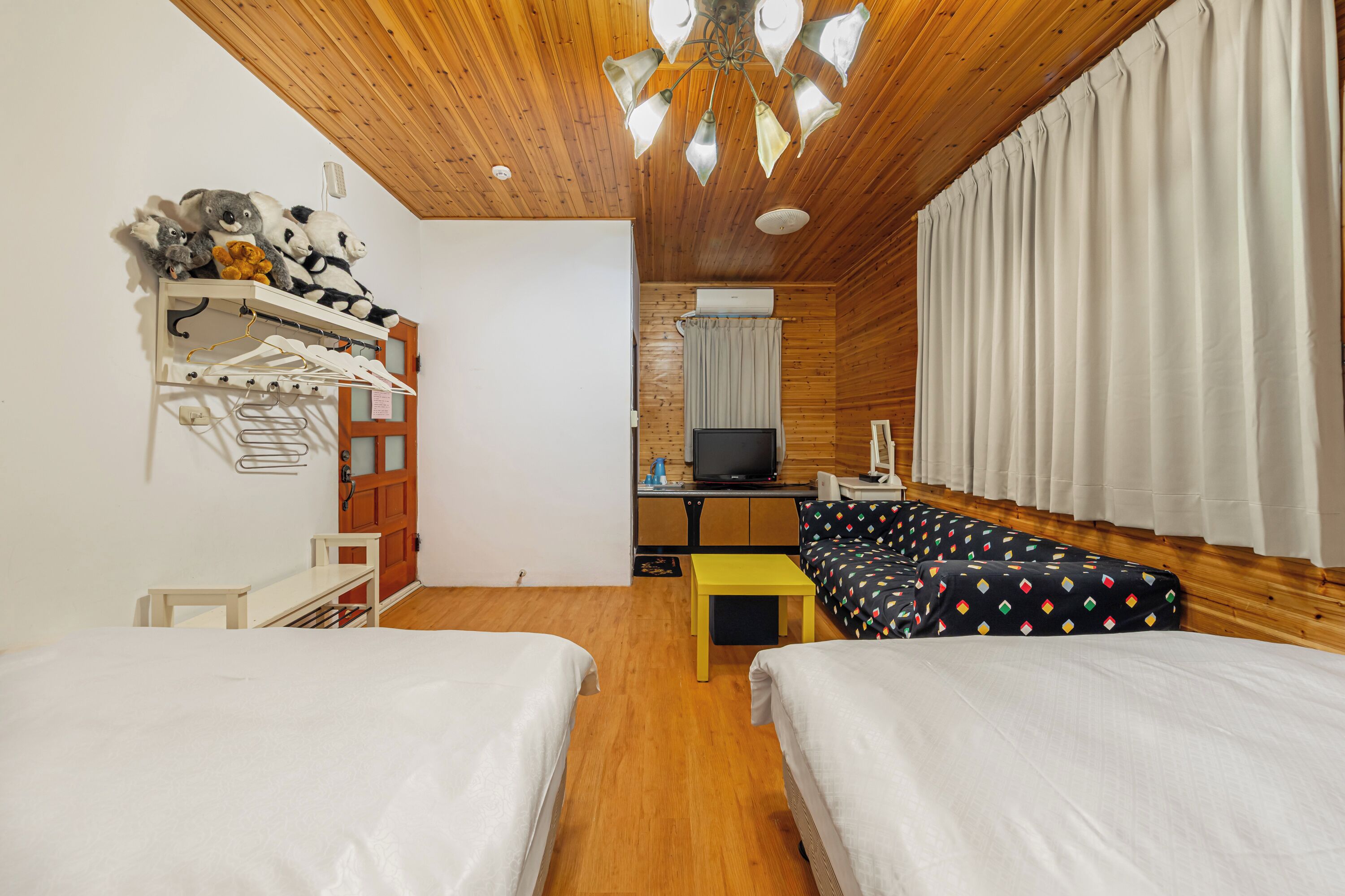 Una habitación con dos camas, televisión, escritorio y estante con peluches.