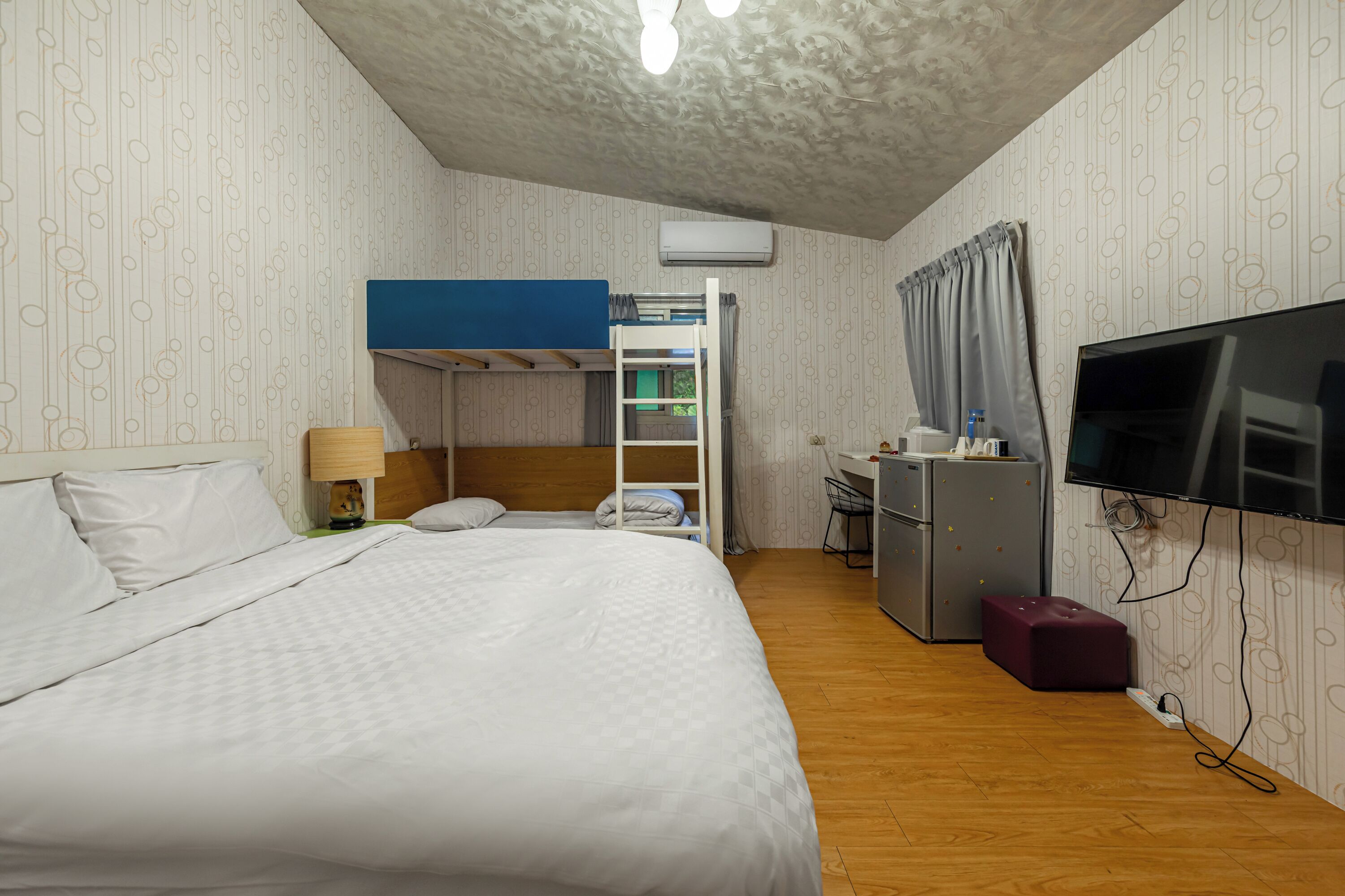 A hotel room with a bunk bed, a desk with a chair, a television, and a small kitchenette.