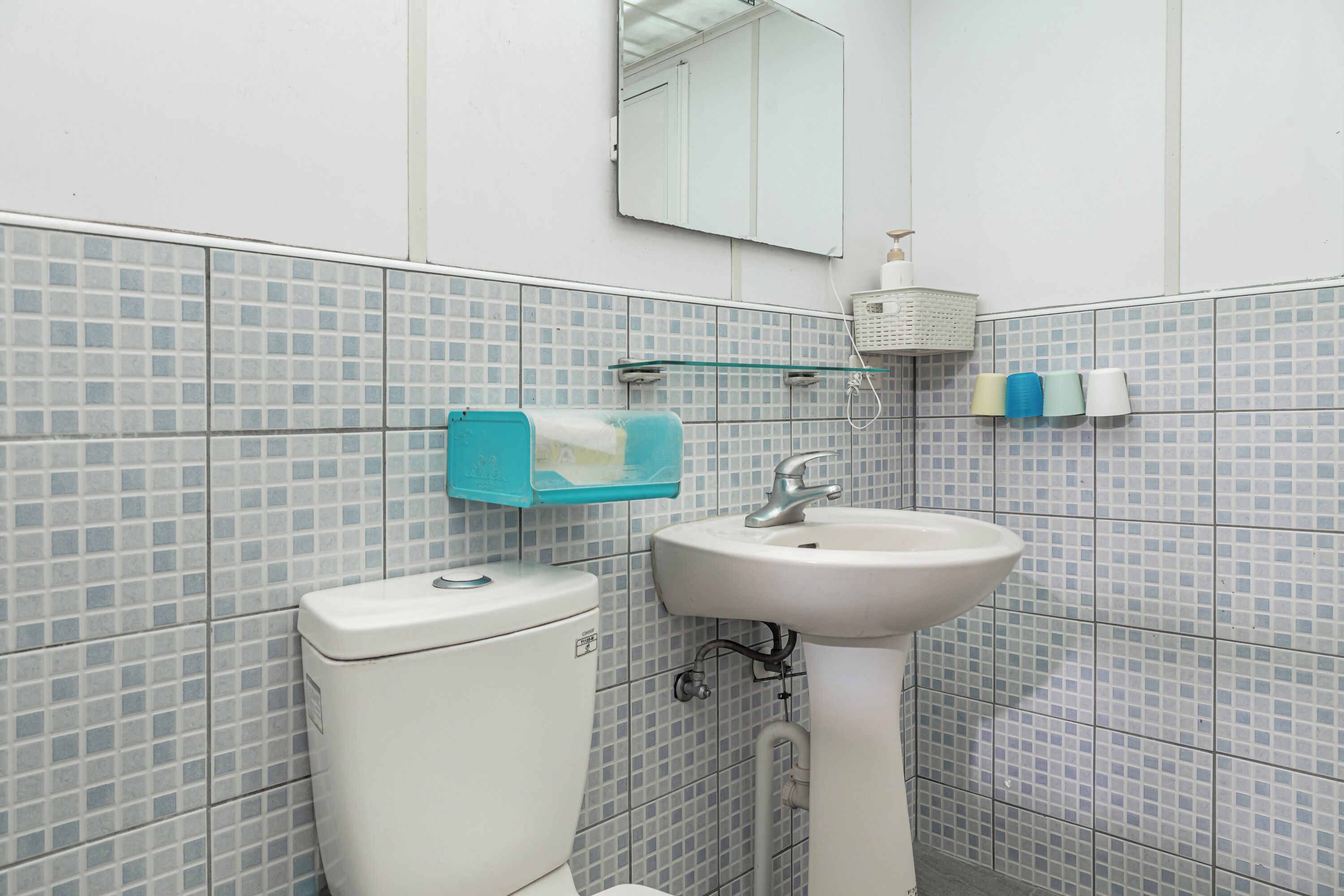 A bathroom with a toilet, sink, mirror, and tiled walls.