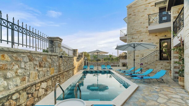Una piscina con sillas de descanso y sombrillas, paredes de piedra y una escalera de piedra.