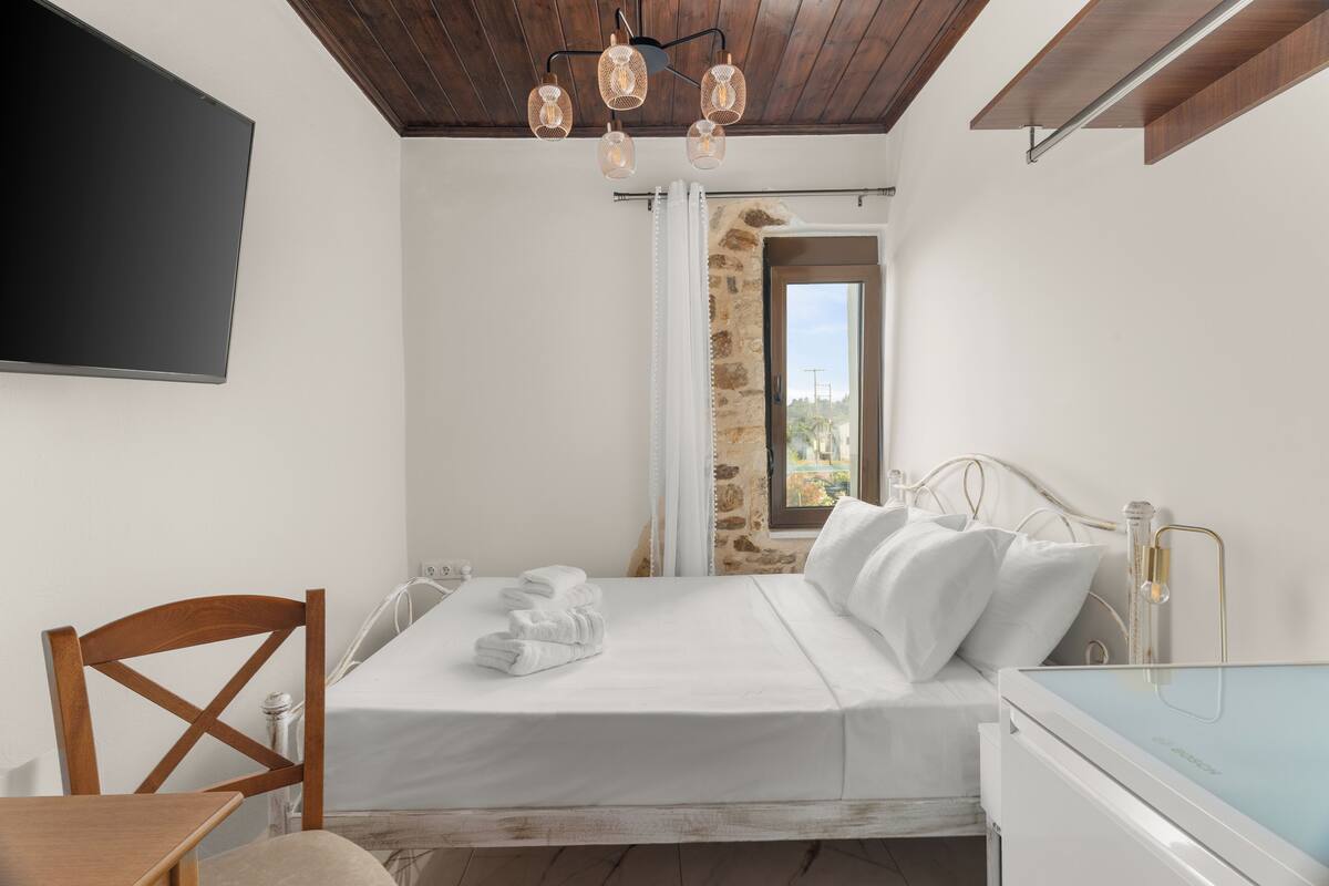 Une chambre à coucher comprenant un lit, une chaise en bois, une table de chevet et un téléviseur fixé au mur.