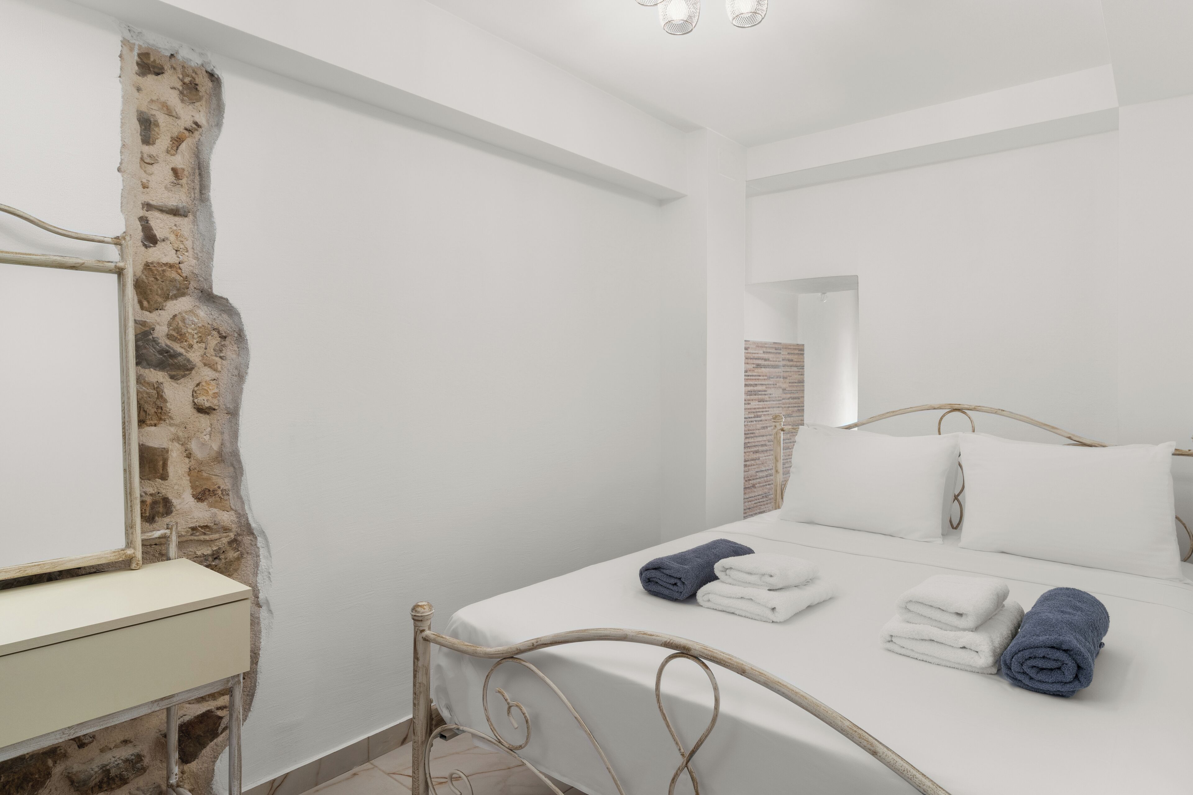 Une chambre avec un mur en pierre, un lit avec des serviettes blanches et bleues, et une table de chevet blanche.