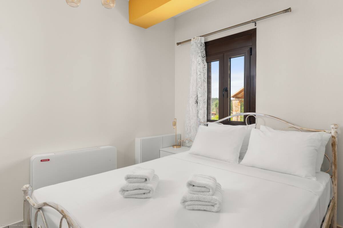 Un lit bien fait, avec du linge de lit et des serviettes blanches, une table de chevet avec une lampe et une fenêtre avec des rideaux.