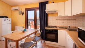Une cuisine compacte équipée d’une cuisinière à gaz, d’un four et d’un lave-vaisselle, une table à manger en bois avec des chaises, et une vue sur l’extérieur grâce à une porte vitrée.