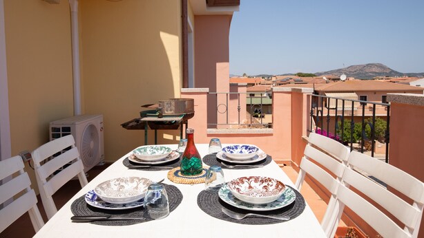 Une table à manger installée sur un balcon, offrant une vue dégagée sur le paysage urbain et les montagnes au loin.