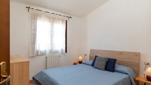 Une chambre à coucher avec un lit, des tables de chevet, une fenêtre avec des rideaux et un radiateur.