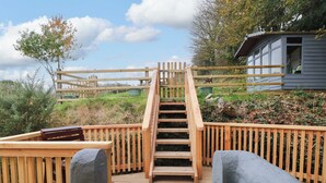 A wooden staircase leading to a deck with a view of a house and surrounding greenery. - Pendre Barn (Llanfyrnach)